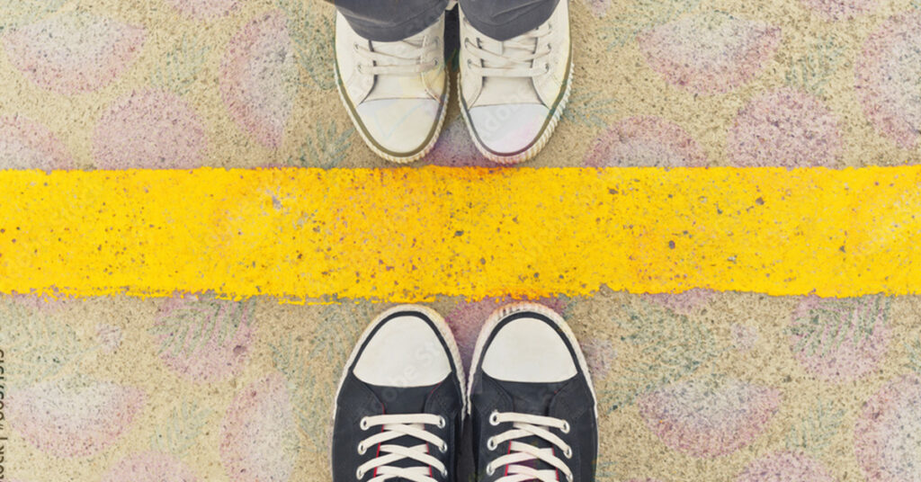 creative business boundaries. Image depicts a line on the ground with two pairs of facing shoes touching the line.