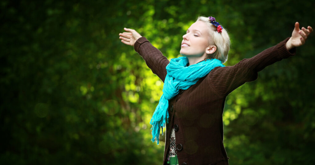 creative business joy. image depicts woman in a forest with arms outstretched and turquoise scarf popping