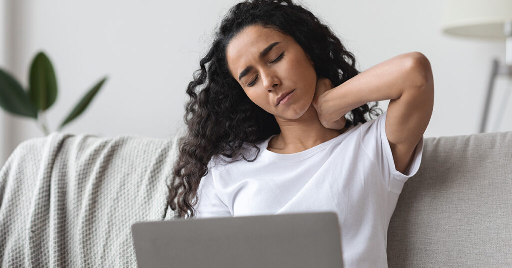 gifts for graphic designers: ice packs, arnica cream, compression gloves. Image depicts woman in front of a laptop holding her neck in pain.