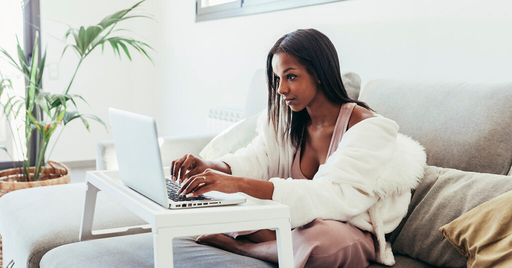 gifts for graphic designers: lapdesk. Image depicts a woman sitting on her couch with a laptop on a lap desk