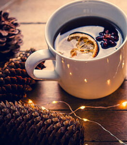 image shows autumn pinecones with twinkling lights by a cup of orange hibiscus tea.