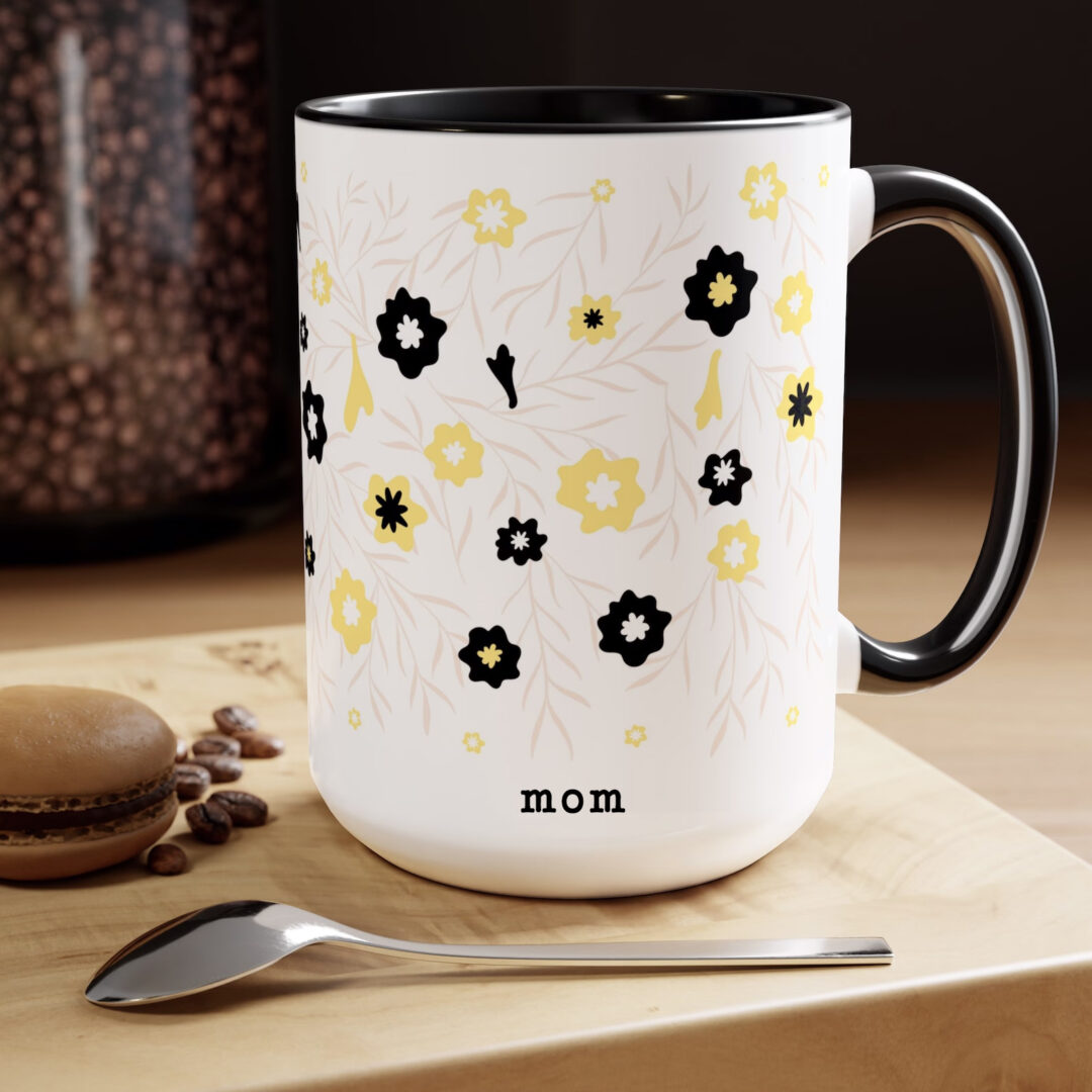 mug shows white ceramic mug with black handle and black inside. Mug is printed with flowers and the word "mom"