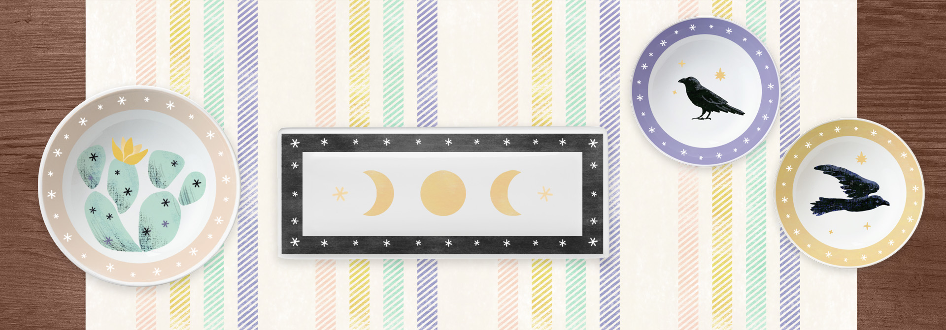alesha-sevy-portfolio Alesha Sevy art - image shows four plates on a striped cloth. Two plates have ravens, one plate has a cactus, one plate has moon phases